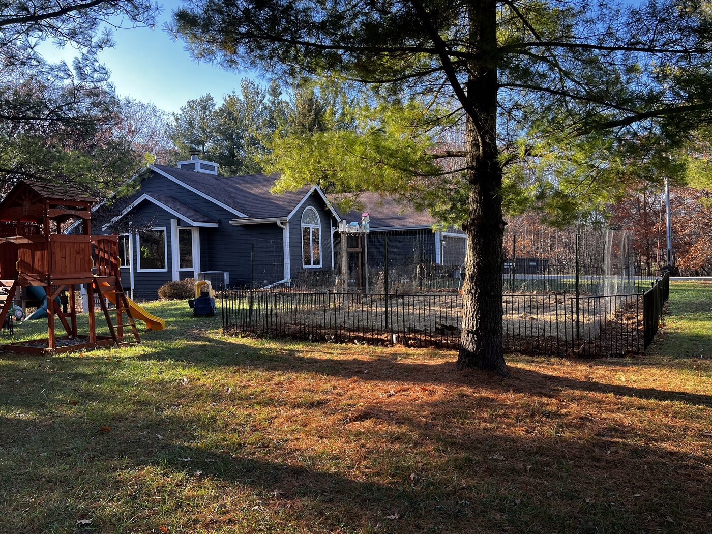 A backyard with a play set and mature trees behind a blue home in the Des Moines metro.